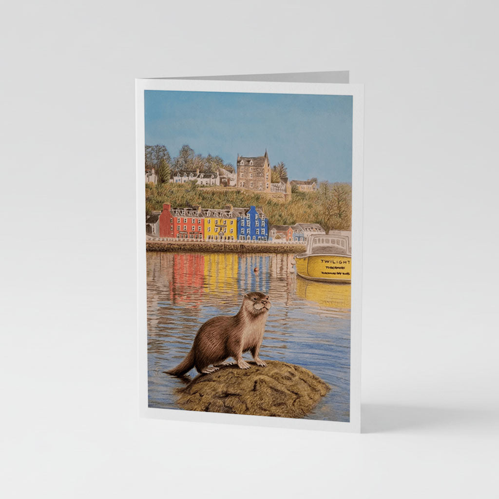 A6 Greetings Card Vertical - Detailed illustration of a brown otter sitting on a rock in Tobermory Bay with colorful red, yellow, and blue waterfront houses and sailing boats in calm blue water beneath a clear sky